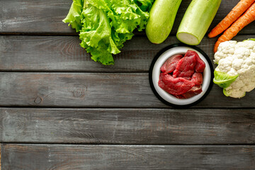 Natural pet food in feeding bowl and ingredients meat and vegetables, top view