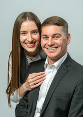 Fashionable man and woman in classic style posing in studio, smiling confidently at camera. Modern couple portrait on white background. Concept of fashion, elegance, and youth.