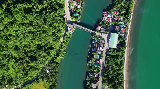 Scenic aerial top-down flyover of coastal barangay town connected to lush, hillside village via river bridge - Batalay, Catanduanes, Philippines