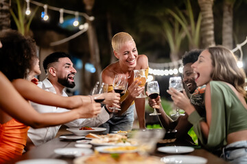 Group of diverse friends raising glasses in a joyful toast at a tropical outdoor party, celebrating together under palm trees and string lights