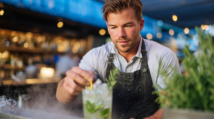 Man in apron preparing kombucha rosemary spritzer, steam from fresh herbs, citrus zest, and cooling mist on glass highlights freshness