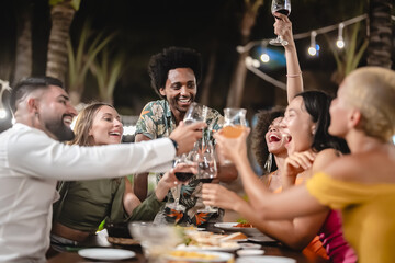 Group of diverse friends raising glasses in a joyful toast at a tropical outdoor party, celebrating together under palm trees and string lights