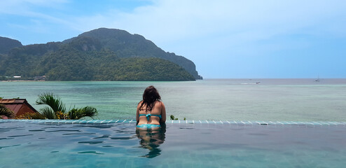 Rear view of young woman bathing in infinity pool contemplating paradisaical sea