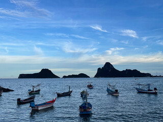 Small fishing boats float on calm waters with rocky islands in the distance under a blue sky with...