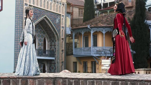 Two beautifull women in a national Georgian dress are dancing in Old Tbilisi city 