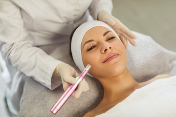 Cosmetologist, dermatologist beautician performing female face microneedling using dermapen for...