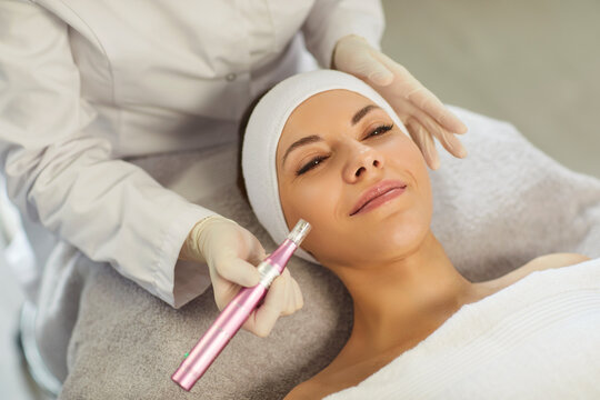 Cosmetologist, dermatologist beautician performing female face microneedling using dermapen for skin care, facial deep cleansing, skincare instrument professional treatments, happy woman enjoying