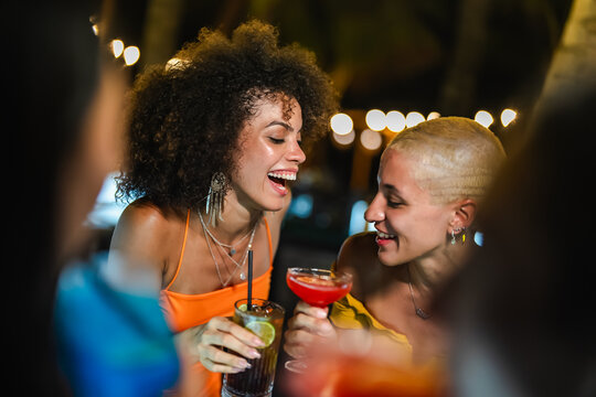 Group of friends toasting with colorful cocktails during a lively night out, showcasing vibrant drinks and festive vibes