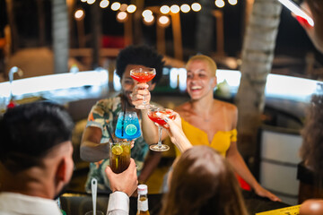 A group of young adults socializing at a lively outdoor bar at night, enjoying colorful cocktails and engaging in cheerful conversation.