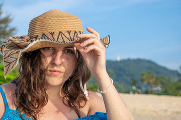 Close up view of young model looking to camera calm with hand on hat on beach
