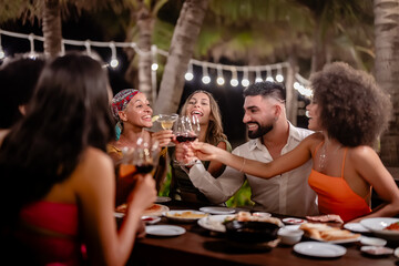 Group of diverse friends raising glasses in a joyful toast at a tropical outdoor party, celebrating together under palm trees and string lights
