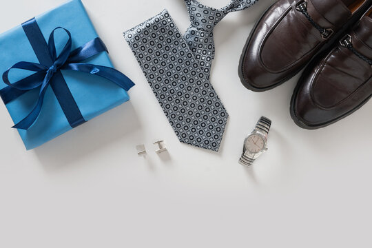 Happy Fathers Day greeting card with gift box. Set of classic mens clothes - brown shoes, wrist watch, necktie and blue gift on gray background. Men's accessories set. Top view. Copy space. - Powered by Adobe