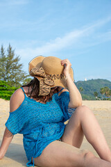 Close up view of young model posing covering his face with hand on hat on beach