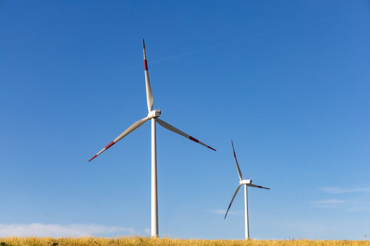 Wind turbines in an open countryside field under a clear blue sky, used for renewable energy production and clean power generation.