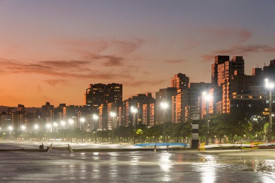 Santos city, Brazil. Waterfront buildings during golden hour. Waterfront gardens, illuminated beach and bridge over water channel No. 6.