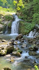 Serene multi-tier waterfall nestled in a lush forest  dappled sunlight illuminates cascading water over mossy rocks, evoking natural tranquility. © Наталя Пасічник