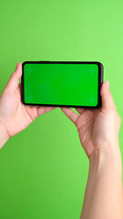 Close-up of hand holding smartphone with green screen in horizontal position against chroma background, ideal for video or landscape app mockups

