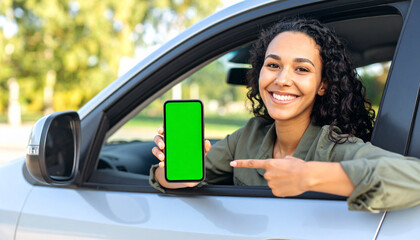 Woman in driver’s seat pointing at smartphone with green screen, showing device to camera, car interior, mobile app mockup concept

