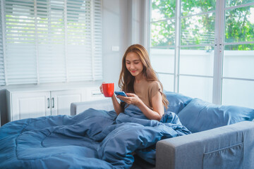 Asian housewife wakes up in the morning, stretching happily on her bed with a blue blanket. Natural...