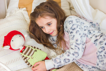 Beautiful little girl in kigurumi pajamas on the bed with her favorite knitted toy