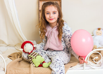 Beautiful little girl in kigurumi pajamas on the bed with her favorite knitted toy