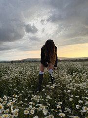 beautiful slavic woman with dark hair in elegant clothes posing in a field of blooming daisies at sunset