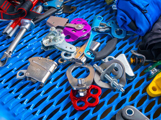 Assortment of climbing and safety hardware including ascenders, pulleys, carabiners, and rope clamps on a blue perforated surface – Climbing, Safety Equipment.