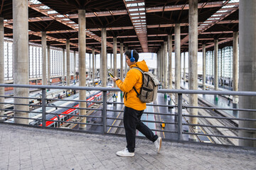 Young traveler walking in train station using smartphone and headphones