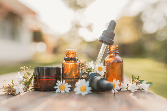 Collection of various amber essential oil bottles in natural outdoor setting with fresh flowers