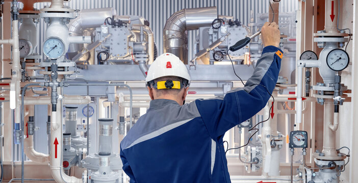 Engineer in protective gear checks pressure gauges and pipeline valves in an industrial facility, ensuring system performance. &ndash; Engineering. Industrial equipment.