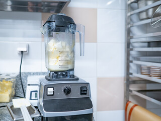 Close-up of a commercial blender filled with cream and butter in a professional kitchen, surrounded by baking tools and ingredients. – Catering. Restaurant. Food Industry.
