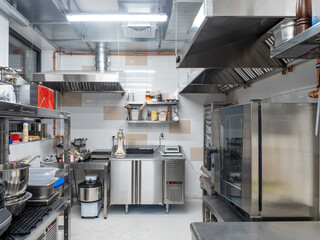 Professional stainless steel kitchen with oven, mixer, ventilation hoods, and workstations equipped...