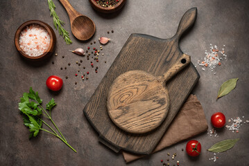 Empty cutting wooden boards, spices and cooking ingredients flat lay on dark rustic background, top view