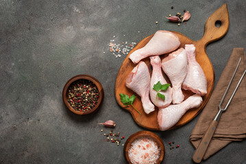Raw chicken legs and spices on dark rustic background, top view, flat lay