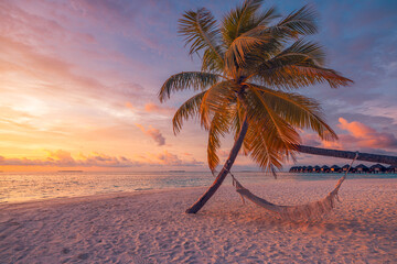 Closeup sunset view palm tree with hammock swing over golden sand sea. Romantic inspire carefree tropical landscape with vivid sky, perfect for summer vacation, relaxation, and dreamy beach background