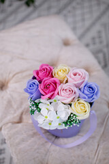 Colorful bouquet of artificial pastel roses and white flowers arranged in a lavender hat box with ribbon. Soft background and cozy light setting