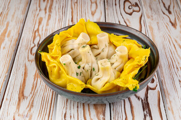 Traditional Georgian khinkali dumplings served in a ceramic bowl, surrounded by bright yellow lavash. Top view on rustic wooden background. Garnished with herbs and spices