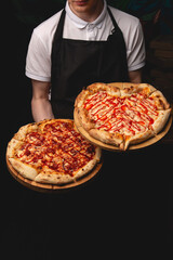 A server in a white polo and black apron presents two freshly baked pizzas. One is a classic...