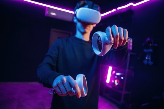 Interacting with game by using controllers. Young man is in virtual reality glasses indoors