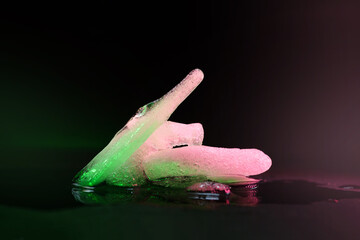 Ice melting. Pieces of melting ice on a dark background. Colored green purple backlight. Selective focus