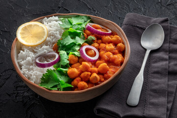 Chana masala, chickpea curry, traditional Indian dish, with fresh cilantro leaves, lemon, and onion, on black