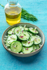 Cucumber salad with dill, red onion, and Feta cheese, on a blue background, with ingredients
