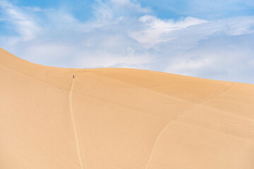 Minimalistic scene with a solitary person hiking on the dunes of Ica desert in Huacachina, Peru