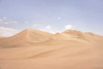 Golden sand dunes under a clear blue sky in Huacachina, Peru,