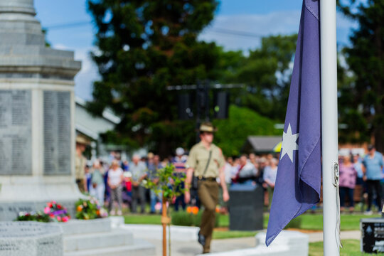 ANZAC day memorial service with focus on flag with cenotaph and soldier in background