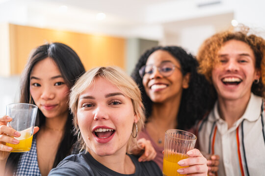 Cheerful multiethnic friends are making a selfie while drinking juice, celebrating and having fun together at home
