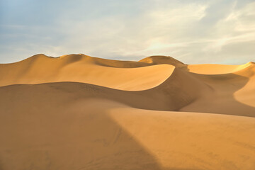 Ica desert landscape at sunset with smooth golden sand dunes near Huacachina, Peru.