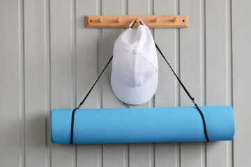 White cap and blue yoga mat hanging on wooden rack against gray wall