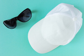 White baseball cap and black sunglasses. Green background. Top view.