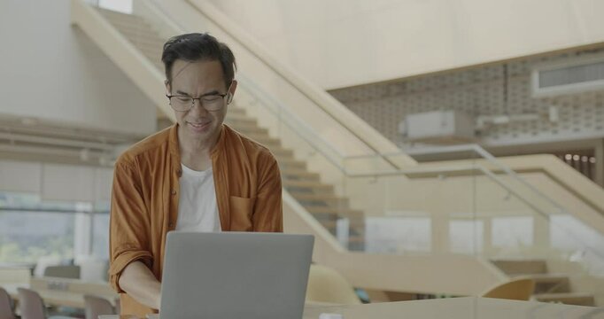 Senior Asian businessman wearing headset celebrates success during online meeting in modern co-working space. Remote work and business communication concept.	
